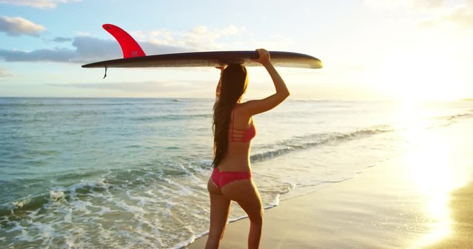 Beautiful surfer girl walking down the beach into the sunset
