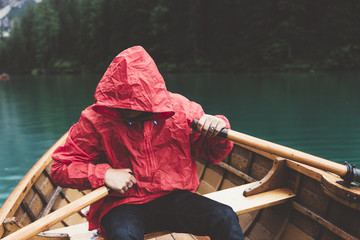 Man with red raincoat rowing a wood boat on Braies lake - 121585747