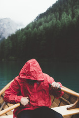 Man with red raincoat rowing a wood boat on Braies lake - 121585911