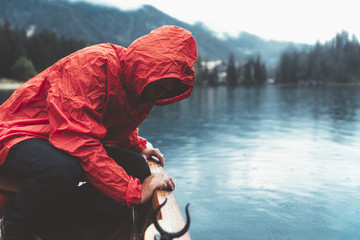 Man with red raincoat is watching the water on a wood boat in Braies lake