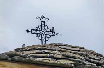 Stone slate-roof of old medieval church with cross in restored Montenegrin or Giginski monastery  St. St. Cosmas and Damian, mountain  Kitka, Breznik, Pernik region, Bulgaria  - obrazy, fototapety, plakaty