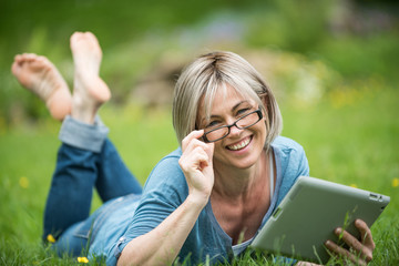 a nice woman of 40 years who is reading her emails in the garden