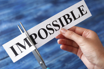 Hand cutting word IMPOSSIBLE on blue wooden background