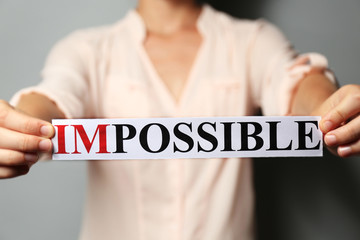 Woman holding word IMPOSSIBLE, close up