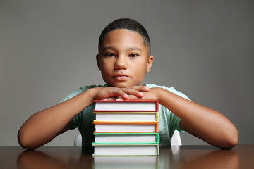 African American boy with books on grey background