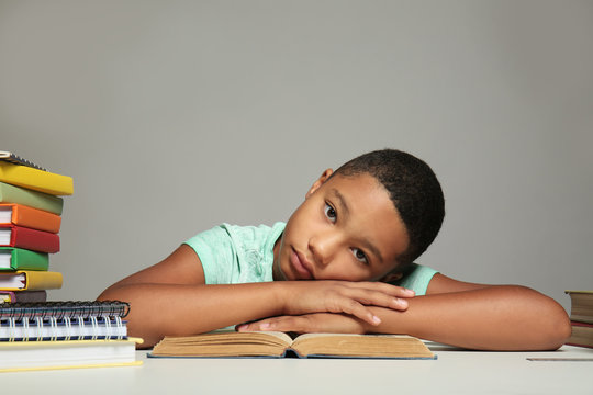 African American boy resting on book on grey background