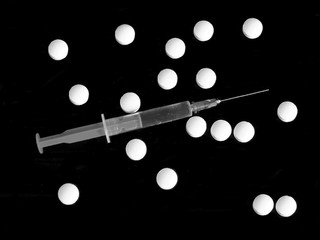 Injection and many drug pills on black background in black and white colors