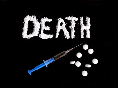Cocaine drug powder in death word shaped, injection and drug pills on black background