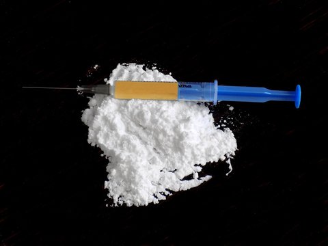 Injection with drug on cocaine drug powder pile on black background
