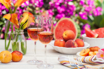 glasses of rose wine, peaches, plums and watermelon at a picnic in the summer