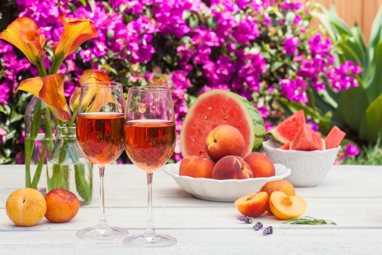 glasses of rose wine, peaches, plums and watermelon at a picnic in the summer