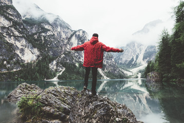 Man with arms up with red raincoat on a rock on Braies lake 