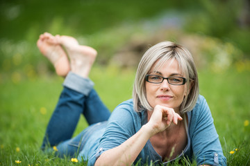  the portrait of a woman of 50 years lying in grass in park