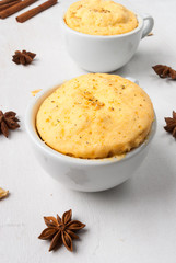 Two pumpkin mug-cakes white coffee cups on a white wooden table, with spices - cinnamon and anise