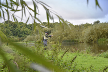 Fototapeta na wymiar Fly-fisherman fishing in river from riverbanks