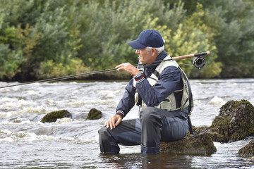 Fly-fisherman waiting with fishing pole on shoulder