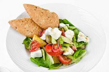 Greek salad with feta cheese, Ligurian olives and tortilla pea and hummus on a plate on a white background, closeup