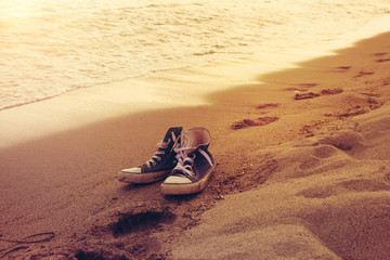 Hipster sneakers in a sea surf on a sand with footprints