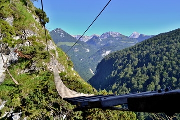 Rope wooden bridge on via ferrata trail in mountains above a forest
