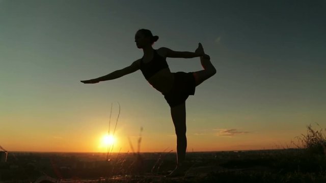 Silhouette of sporty woman practicing yoga in the park at sunset - lord of the dance pose. Sunset light, golden hour. Freedom, health and yoga concept