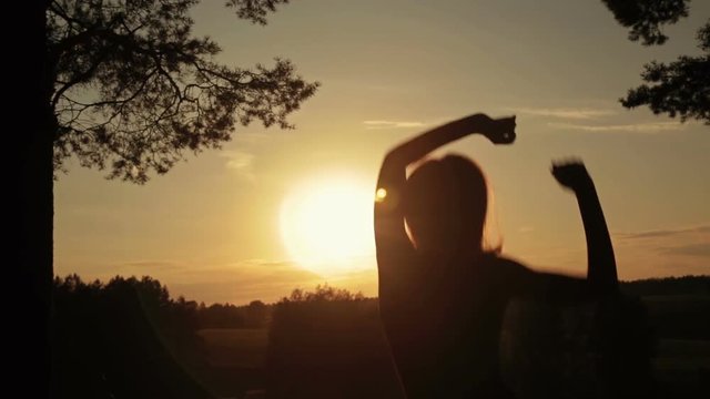 Young happy woman jumping, dancing and having fun in the forest at sunset. Silhouette of woman. Sunset light, sun lens flares, golden hour. Freedom and happiness concept