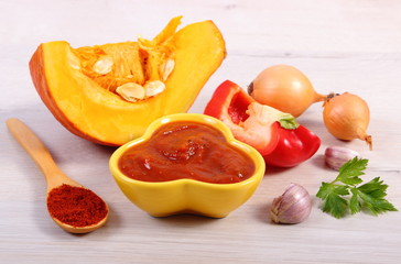 Sauce of pumpkin in glass bowl, spices and ingredients on wooden table