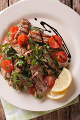 Warm salad of grilled beef with arugula and tomatoes close-up. Vertical top view
