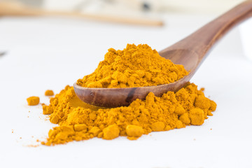 Turmeric powder in wood spoon on white background