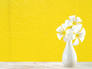 white plumeria bouquet in simple vase on desk floor with bright yellow wall