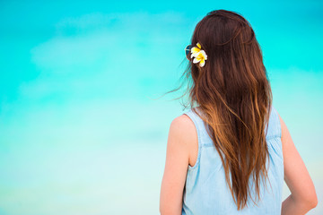 Naklejka premium Young beautiful woman during tropical beach vacation. Enjoy suumer vacation alone on the beach with frangipani flowers in her hair