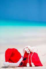 Closeup of red Santa bag and Santa Claus hat on beach. Xmas travel vacation and travel cuprise concept. Beach accessories with Santa Hat on white tropical beach