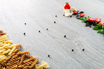 Mixed of two colored pasta near tomatoes, garlic and basil on grey wooden  background. Raw  frame. Copy space.