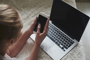 Top view of girl lying on the bed next to the computer and holding a mobile phone