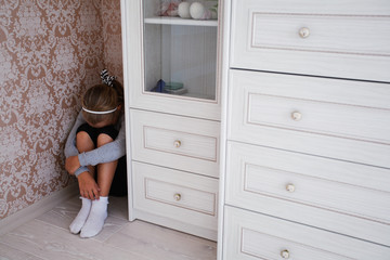Little aggrieved girl sitting in the corner of her room  behind the cupboard