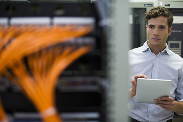 Computer technician using digital tablet performing maintenance check of mainframe equipment