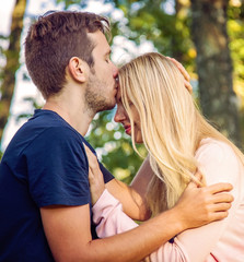 Fototapeta premium Young man kissing his woman's forehead in the park in the summer.