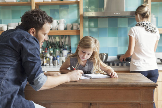 Father teaching his daughter, mother cooking in background
