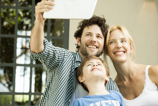 Family with one child posing for selfie taken with digital tablet