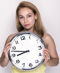 Beautiful young woman looking at a large silver retro clock that she is holding, she wonders how...