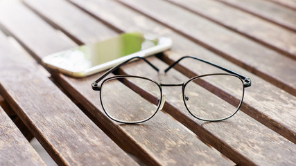 smartphone and glasses on the wood table, vintage style.