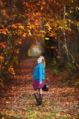 Alone young woman with violin case by country road autumn park. Country music concept. Fallen leaves of forest trees