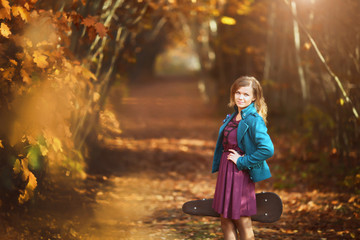 Naklejka premium Alone young woman with violin case by country road autumn park. Country music concept. Fallen leaves of forest trees