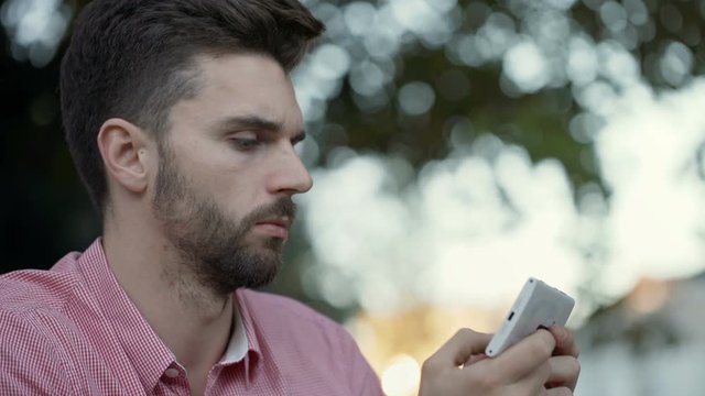 Thoughtful man sitting outdoor and texting on smartphone
