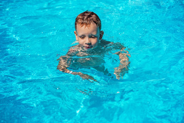 Happy kid playing in blue water of swimming pool on a tropical r