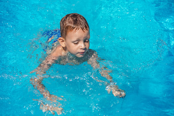 Happy kid playing in blue water of swimming pool.