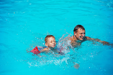 Happy boy enjoying with swimming and splashing with his father.