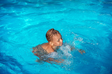 Fototapeta na wymiar Happy kid playing in blue water of swimming pool.