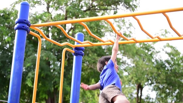 Slow motion, Young asian boy hang the yellow bar by his hand to exercise at out door playground under the big tree