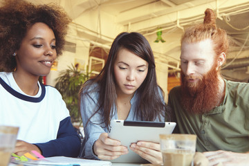 People, innovations and technology. Businesspeople studying financial data on touch pad pc with concentrated look. Attractive Asian girl holding digital tablet sitting at cafe with her partners