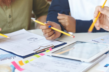 Cropped view of students working on collaborative project at canteen, making research, studying statistics and diagrams on electronic tablet, making changes and amendmends in notes using pencils